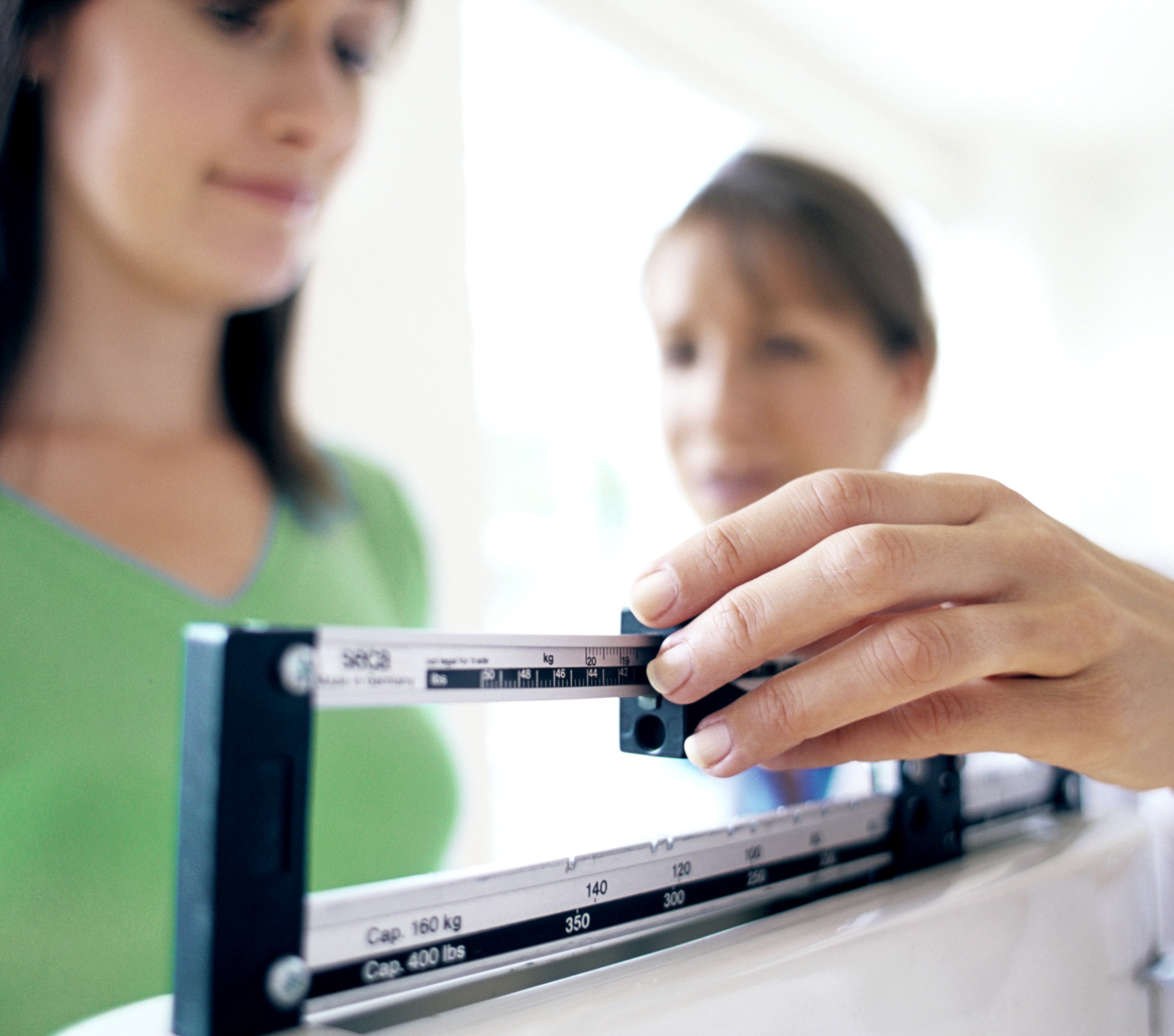 A patient being weighed on a clinical balance beam scale during a medical weight loss appointment